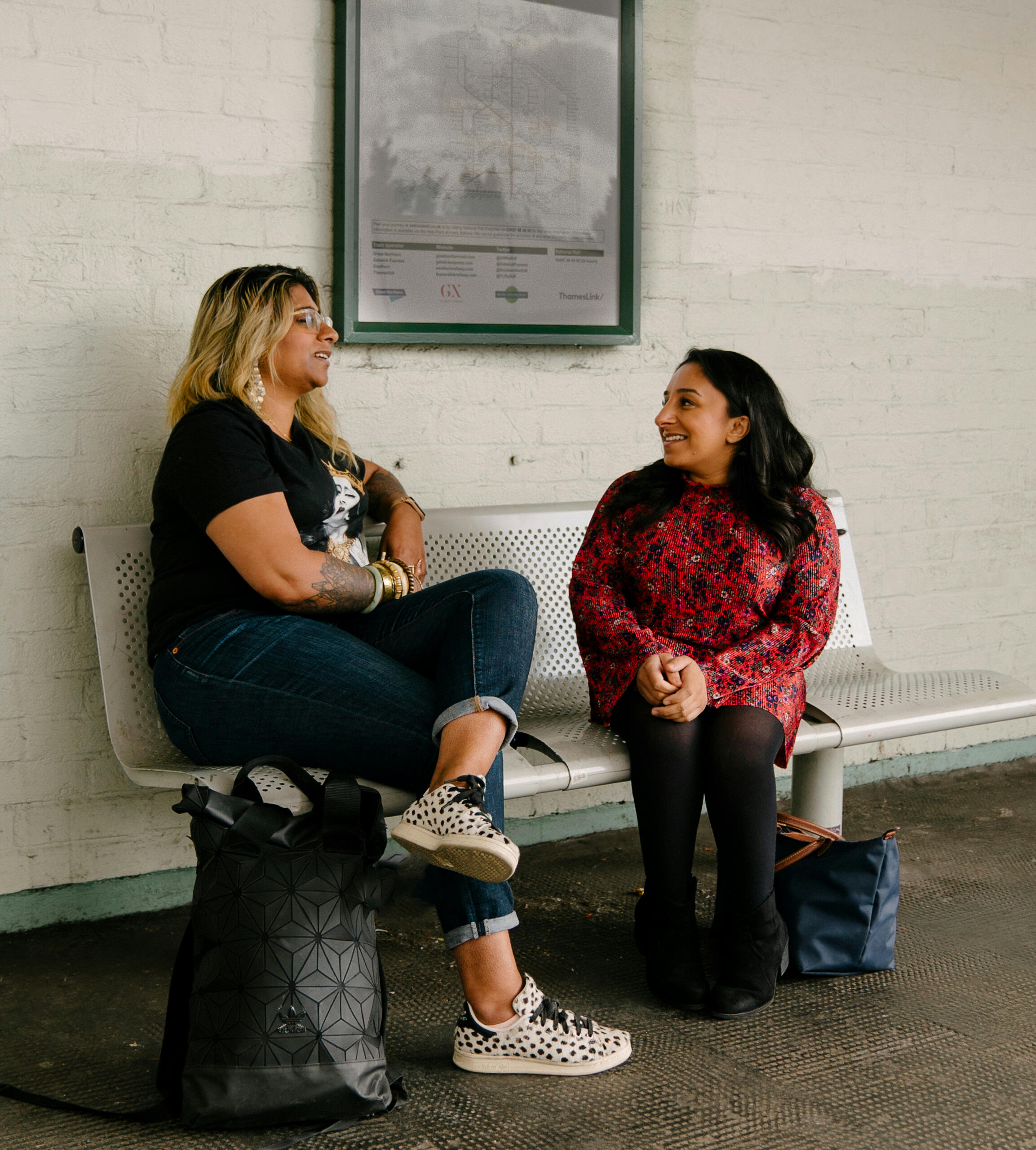 “Two women sitting together at a bus stop, sharing conversation and support, reflecting community, dignity, and connection for women in transition.”